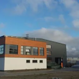 Nowoczesny budynek przemysłowy z elementami cegły i szarej blachy na elewacji, widok z zewnątrz, błękitne niebo z chmurami w tle, elementy konstrukcyjne na placu.