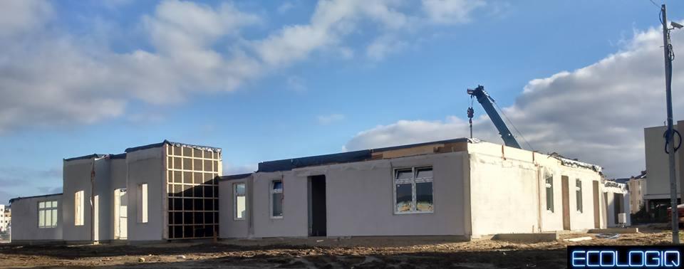 Budowa domu modułowego w trakcie: widoczne ściany, okna, elementy konstrukcyjne i żuraw na tle błękitnego nieba. Etap surowy zamknięty, bez elewacji.