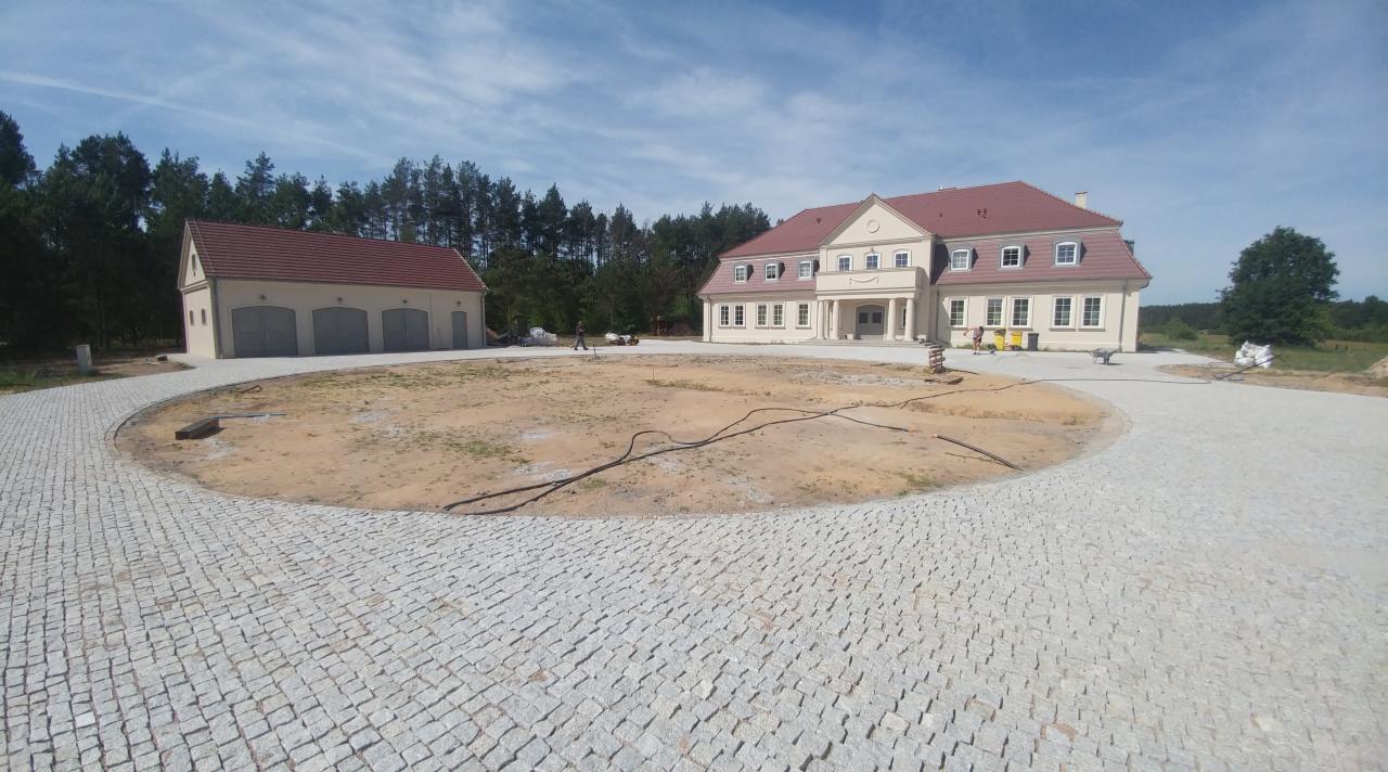 Rozległa posesja z nowo ułożoną, okrągłą kostką granitową prowadzącą do domu i garażu, teren w trakcie prac wykończeniowych.