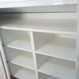 Biała szafa wnękowa z przesuwnymi drzwiami, widoczne puste półki wewnątrz, minimalistyczny design.