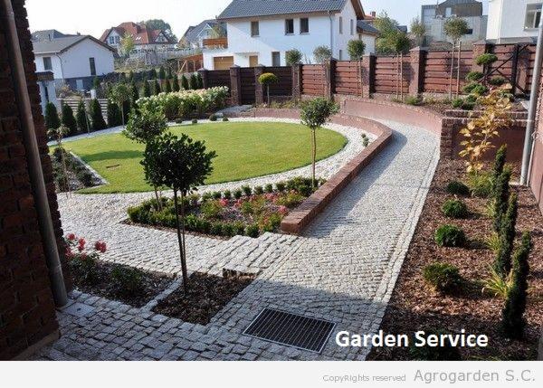 Aranżacja ogrodu z trawnikiem, ścieżką z kostki granitowej i rabatami kwiatowymi, otoczona tujami i ogrodzeniem z drewnianymi panelami.