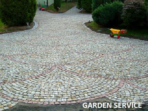 Ułożona z kostki granitowej ścieżka ogrodowa z dekoracyjnym wzorem w kształcie wachlarza, z widoczną dziecięcą taczką w tle.