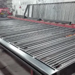 Metalowa konstrukcja bramy wjazdowej z okrągłych prętów, w warsztacie. Czerwona drabina i narzędzia w tle. Surowy stan przed malowaniem.