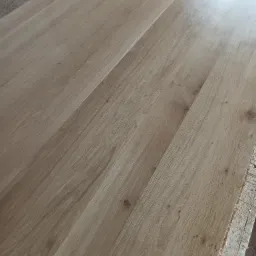 Jasny, dębowy blat z widocznym usłojeniem, leżący na stole roboczym z resztkami obróbki drewna.