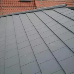 Szary dach z dach&oacute;wki ceramicznej, widok z g&oacute;ry, częściowo widoczny dach sąsiedniego budynku z czerwonej dach&oacute;wki.