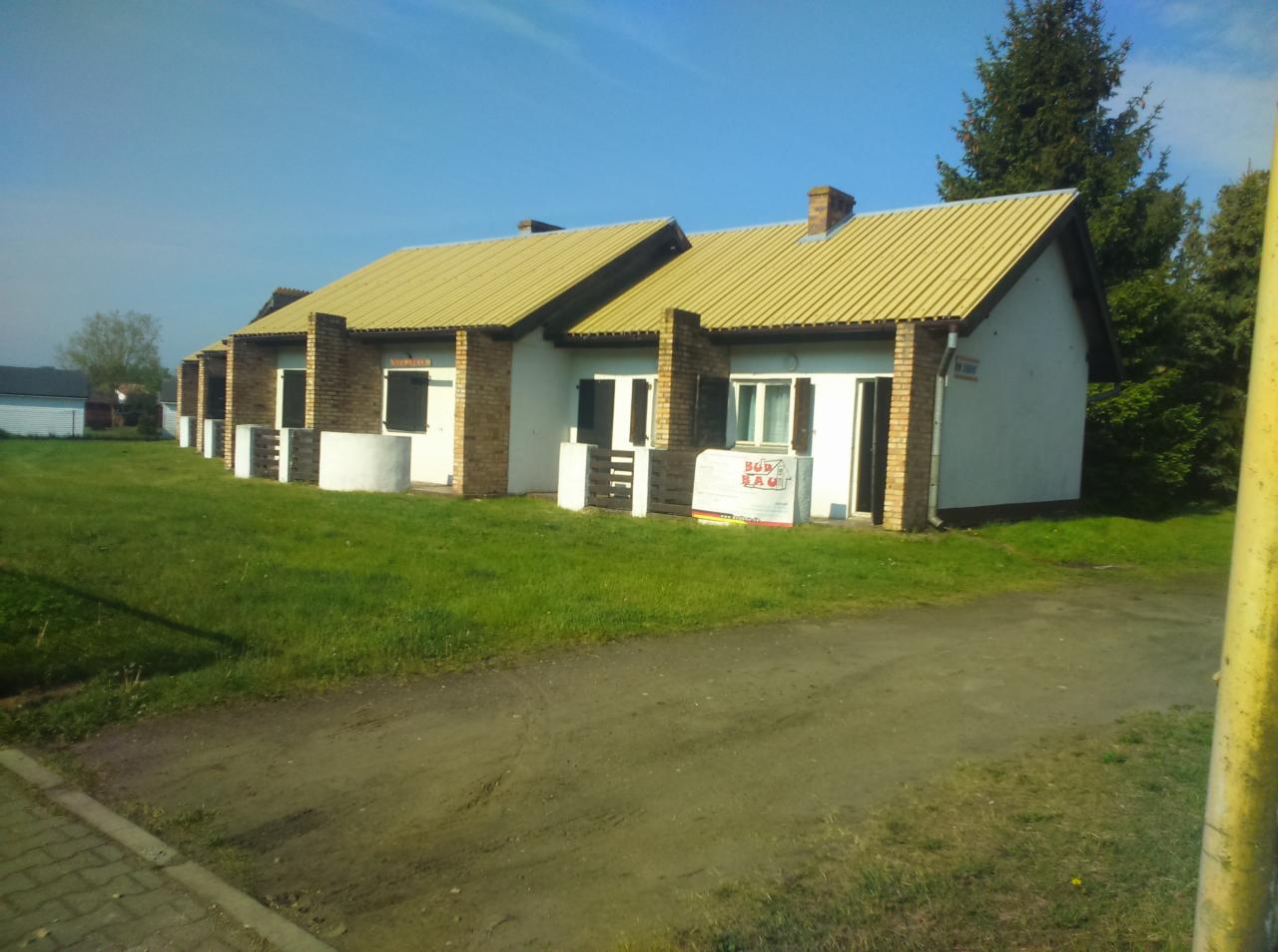 Szeregowe domki jednorodzinne z ceglanymi elementami elewacji i żółtymi dachami, widoczne płyty ociepleniowe przy jednym z wejść.