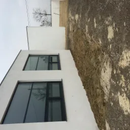 Nowoczesny budynek z dużymi oknami w czarnych ramach. Minimalistyczna architektura, biała fasada, widok z dołu, odbicie drzewa w szybach.