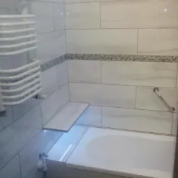 Wykończona łazienka z wanną obudowaną płytkami, p&oacute;łką z podświetleniem LED, grzejnikiem drabinkowym i dekoracyjnym pasem mozaiki na ścianie.