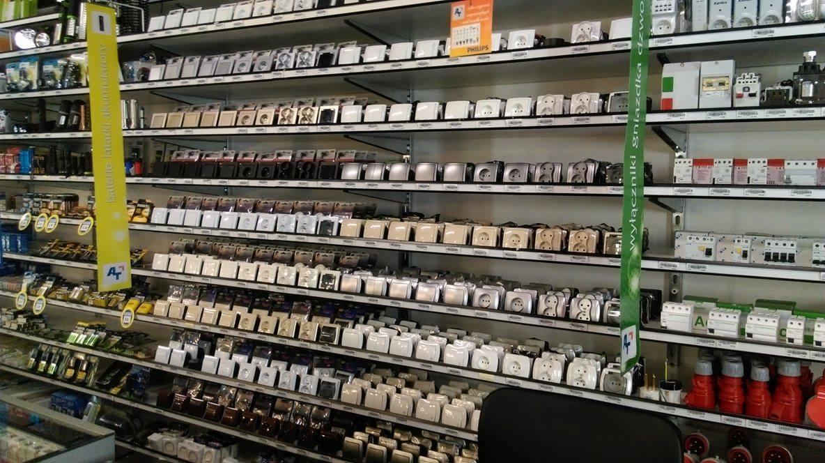 Półki sklepowe wypełnione różnorodnymi gniazdkami elektrycznymi, włącznikami i akcesoriami elektrycznymi, z widocznymi etykietami i oznaczeniami producentów.