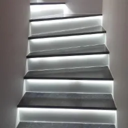 Schody z szarego kamienia z podświetleniem LED na każdym stopniu, widok z dołu, z włącznikiem światła na ścianie.