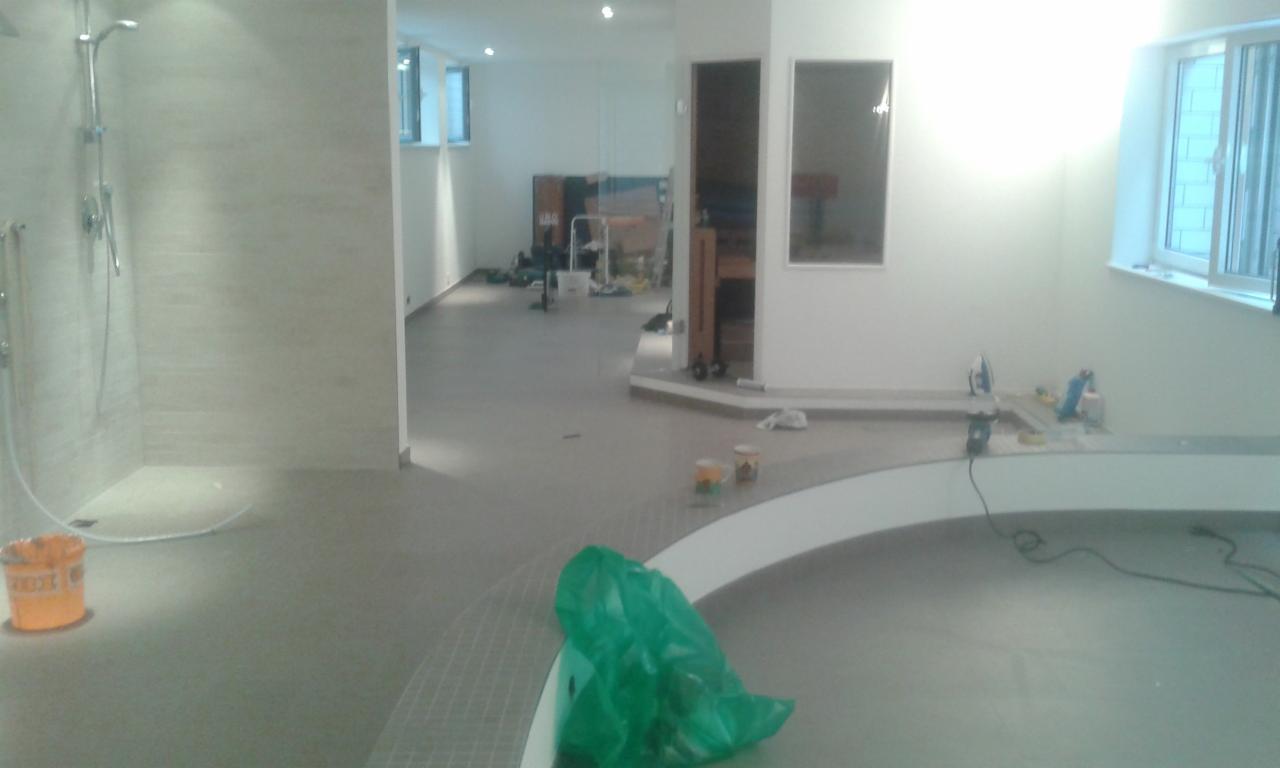 Wnętrze łazienki w trakcie remontu: widoczna kabina prysznicowa z szarymi płytkami, przygotowane podłoże pod wylewkę i narzędzia budowlane. Prace wykończeniowe w toku.