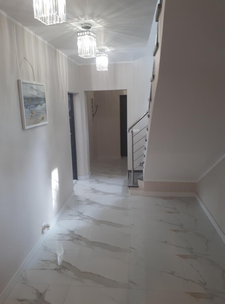 Nowoczesny korytarz z białymi marmurowymi płytkami podłogowymi, szklanymi lampami sufitowymi i schodami z metalową balustradą.