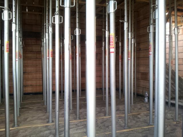 Wnętrze w trakcie budowy: ściany z pustaków i liczne metalowe stemple podtrzymujące strop. Widoczne drewniane podkłady pod stemplami.