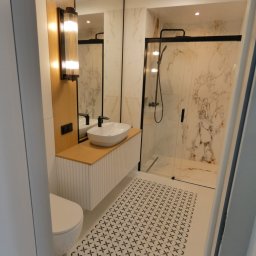 Gładko.pl - Nowoczesna łazienka z kabiną prysznicową typu walk-in, umywalką nablatową na szafce z ryflowanym frontem, oświetleniem ściennym i podłogą w biało-czarne wzory.