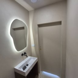 MicroForm Studio - Nowoczesna łazienka w beżowych tonacjach z asymetrycznym lustrem podświetlanym LED i minimalistyczną umywalką nablatową. Ściany wykończone gładzią.
