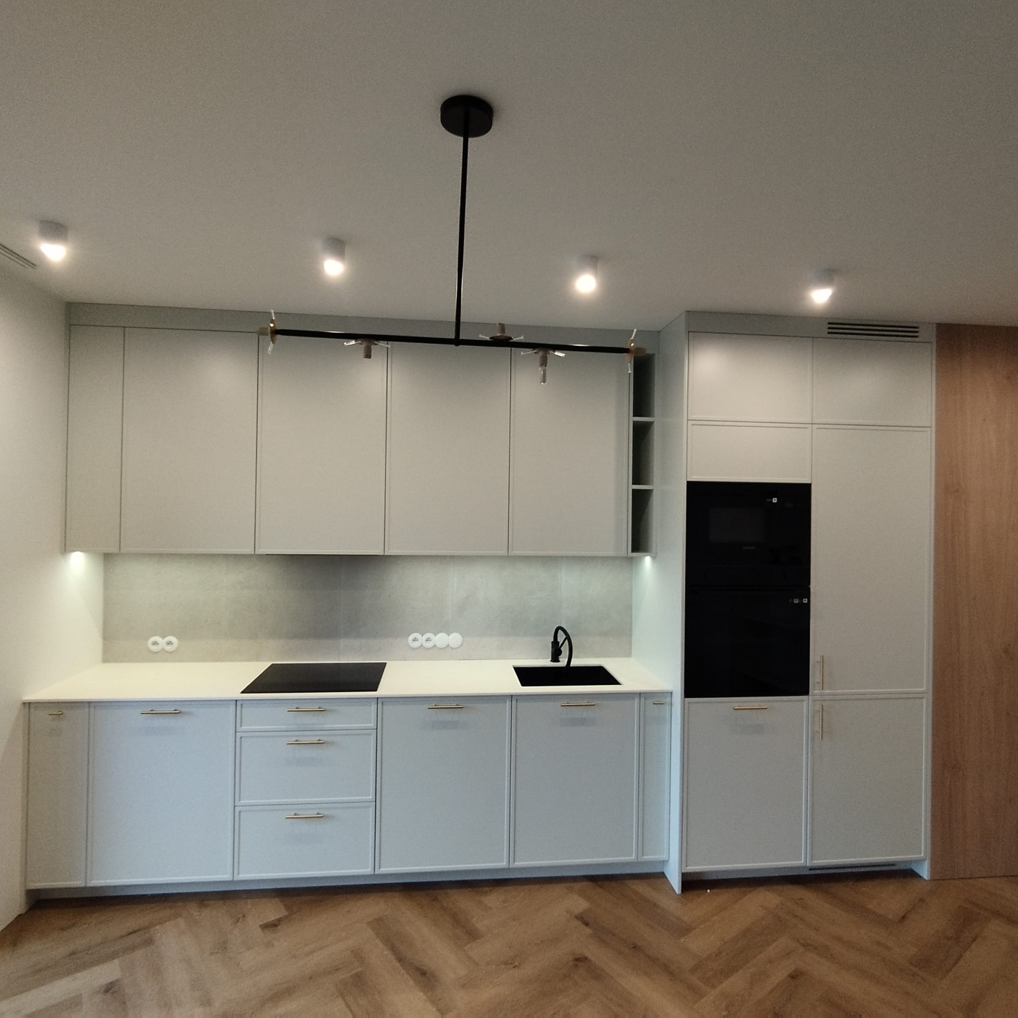 Nowoczesna kuchnia z szarymi szafkami, czarną armaturą i oświetleniem punktowym, parkiet w jodełkę.