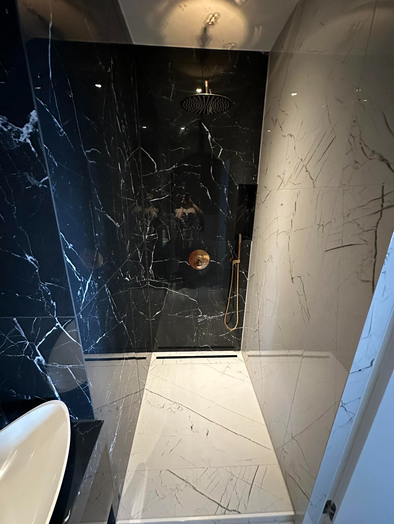 Nowoczesna łazienka z czarno-białymi marmurowymi płytkami, złotą armaturą i deszczownicą, widok z góry.