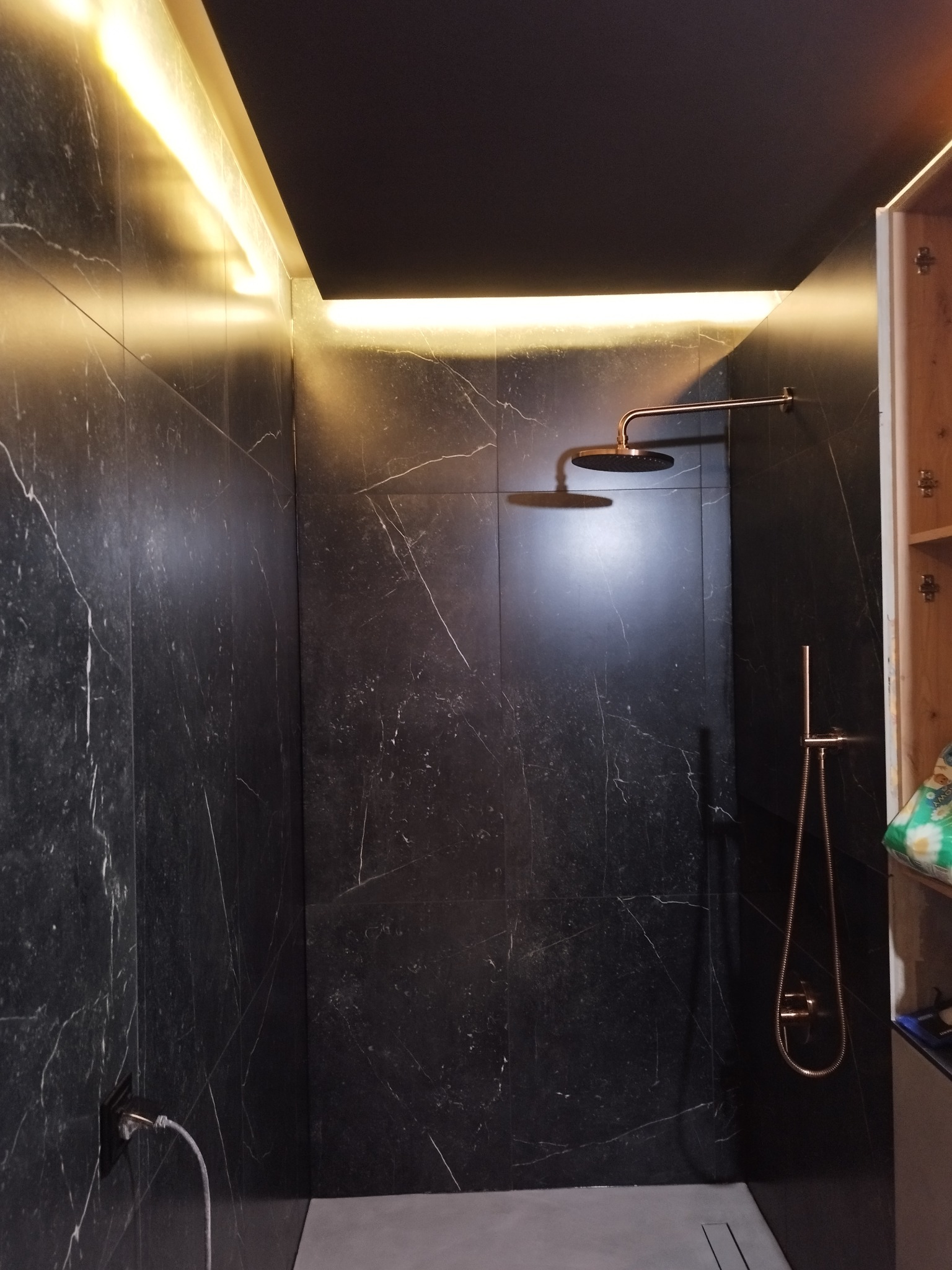 Nowoczesna kabina prysznicowa z czarnymi marmurkowymi płytkami, oświetleniem LED w suficie i miedzianą armaturą.