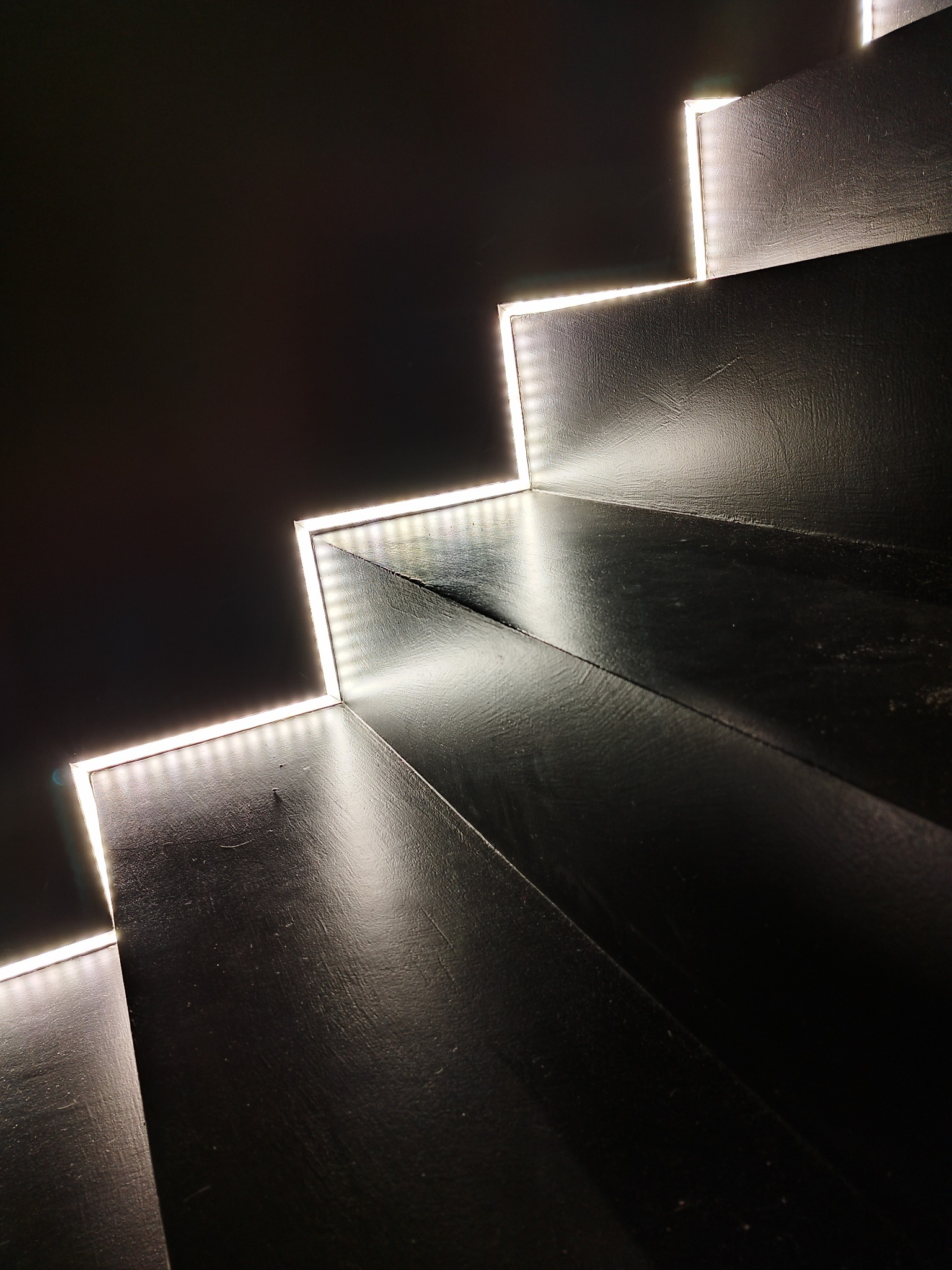 Czarne schody z podświetleniem LED na krawędziach stopni, tworzące nowoczesny efekt wizualny.
