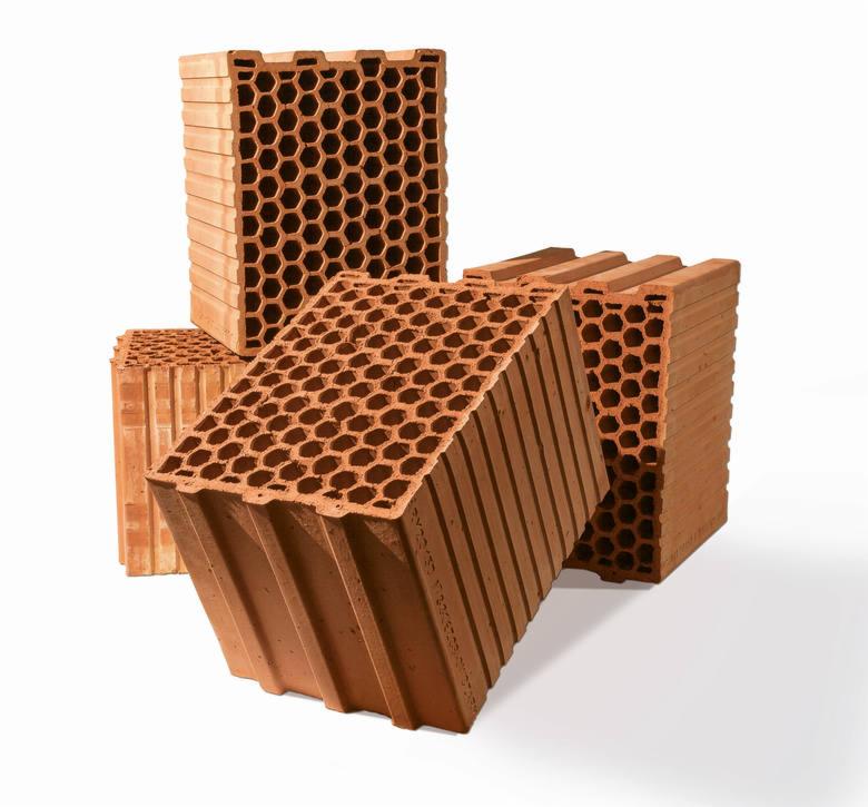 Cegły ceramiczne z otworami o strukturze plastra miodu, ułożone w stos na białym tle, z widocznym cieniem.