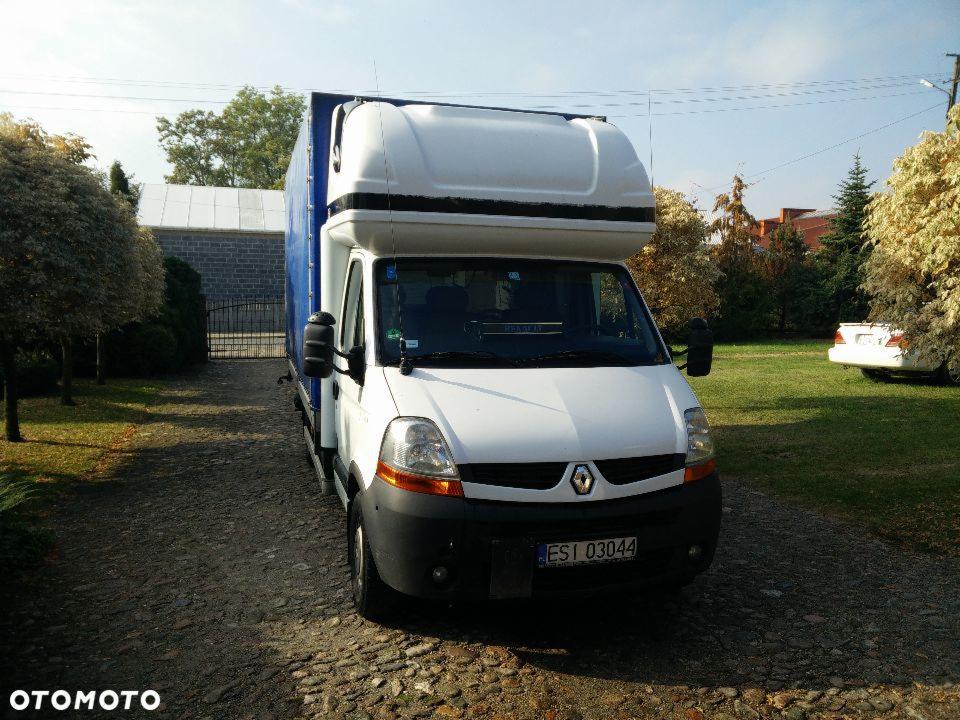 Biały bus Renault Master z wysoką zabudową i niebieską plandeką, zaparkowany na żwirowej drodze. Widoczny numer rejestracyjny ESI 03044. W tle zieleń i budynek.