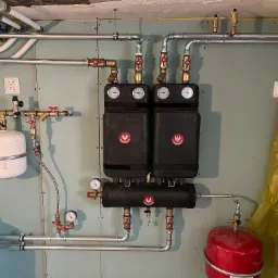 Rozdzielacz ogrzewania podłogowego z dwoma modułami, manometrami i licznymi rurami, zamontowany na ścianie wykończonej płytami gipsowymi.