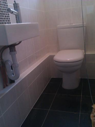 Wykończona łazienka w London z czarną podłogą i jasnymi płytkami ściennymi. Umywalka z chromowaną baterią i toaleta w tle. Minimalistyczny design.