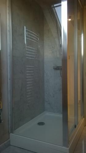 Szklana kabina prysznicowa z grzejnikiem drabinkowym na marmurowej ścianie, oświetlona światłem z okna dachowego. Nowoczesna aranżacja łazienki.