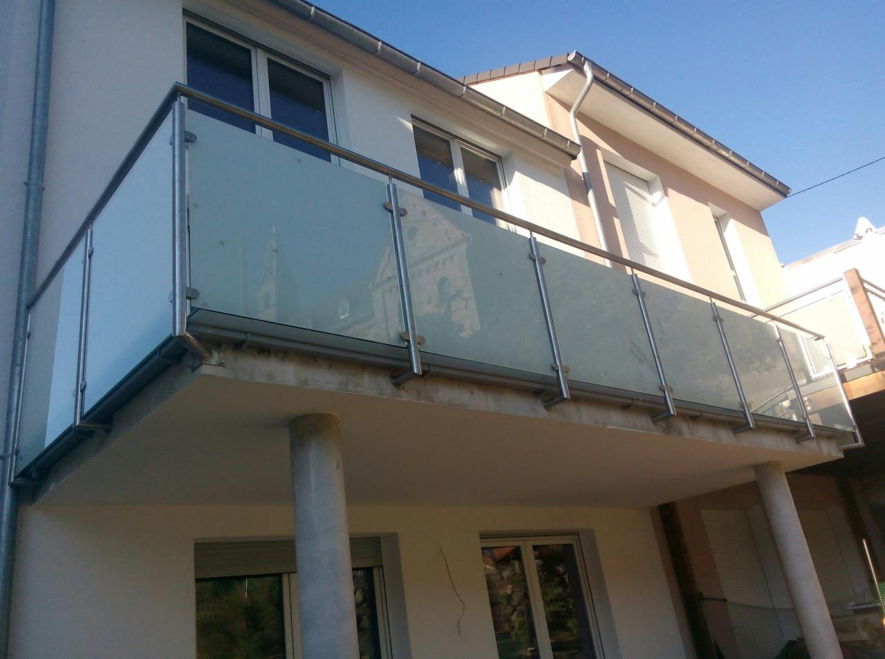 Balkon z nowoczesną szklaną balustradą z elementami ze stali nierdzewnej, widok z dołu, na szkle odbija się budynek.