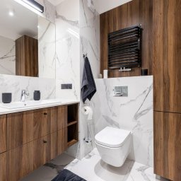 PracowniaARD - Nowoczesna łazienka z marmurowymi płytkami, drewnianymi szafkami pod umywalką, wiszącą toaletą i czarnym grzejnikiem drabinkowym.