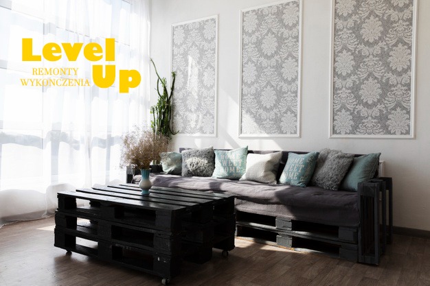 Salon z kanapą i stolikiem kawowym wykonanymi z palet, ściany zdobią dekoracyjne panele w ramkach z motywem ornamentów.