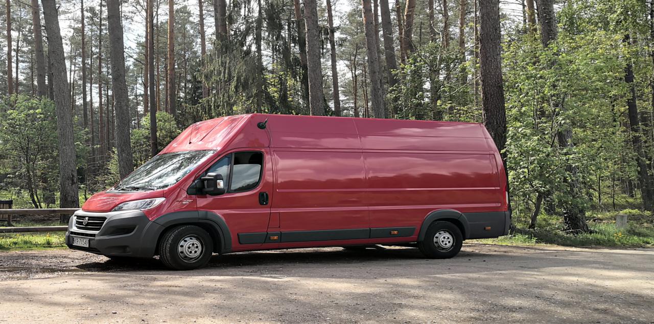 Czerwony bus dostawczy zaparkowany na leśnym parkingu, widoczne drzewa w tle