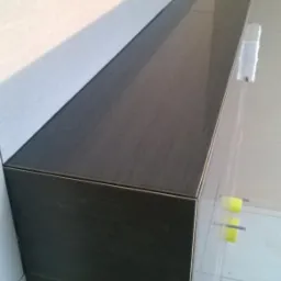 Wykończona półka z ciemnych płytek w łazience, z widocznymi jasnymi płytkami na ścianie i podłodze. Detal wykończenia z bliska, z zachowaniem minimalnych fug.