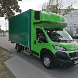 Zielony samochód dostawczy z plandeką na parkingu miejskim, widok z boku, tablica rejestracyjna WE 141VC.