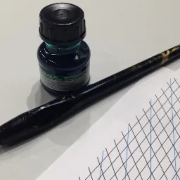 Kałamarz z niebieskim atramentem, pióro ze stalówką i kartka papieru z siatką linii w kolorze czarnym i niebieskim.