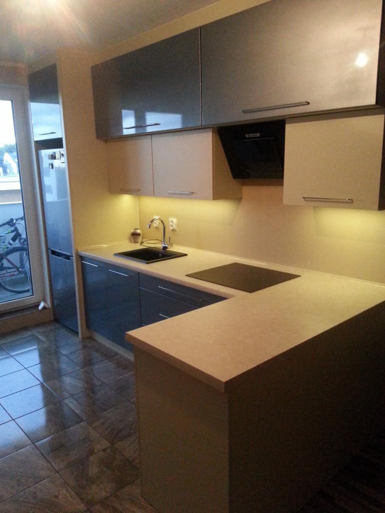 Nowoczesna kuchnia z szarymi i beżowymi frontami szafek, czarnym blatem kuchenki i zlewozmywakiem, oświetleniem LED i błyszczącą podłogą z płytek.