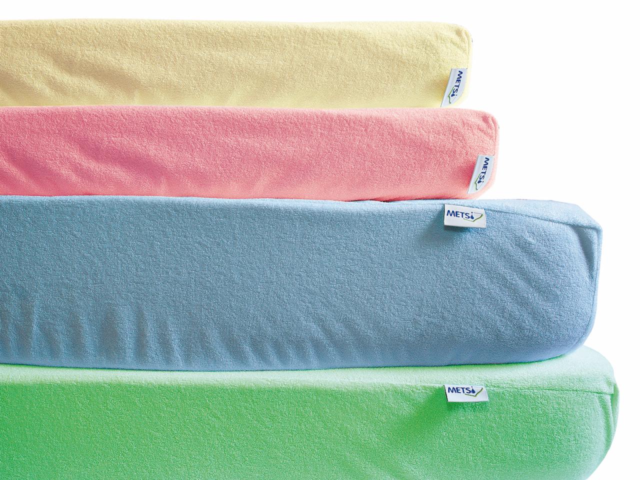 Stos poduszek dekoracyjnych w pastelowych kolorach: żółtym, różowym, błękitnym i zielonym. Poduszki z miękkiej tkaniny z widocznymi metkami producenta.