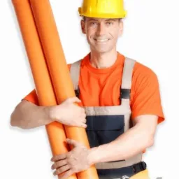 Uśmiechnięty hydraulik w żółtym kasku, trzymający dwie pomarańczowe rury PVC w kombinezonie roboczym na białym tle.