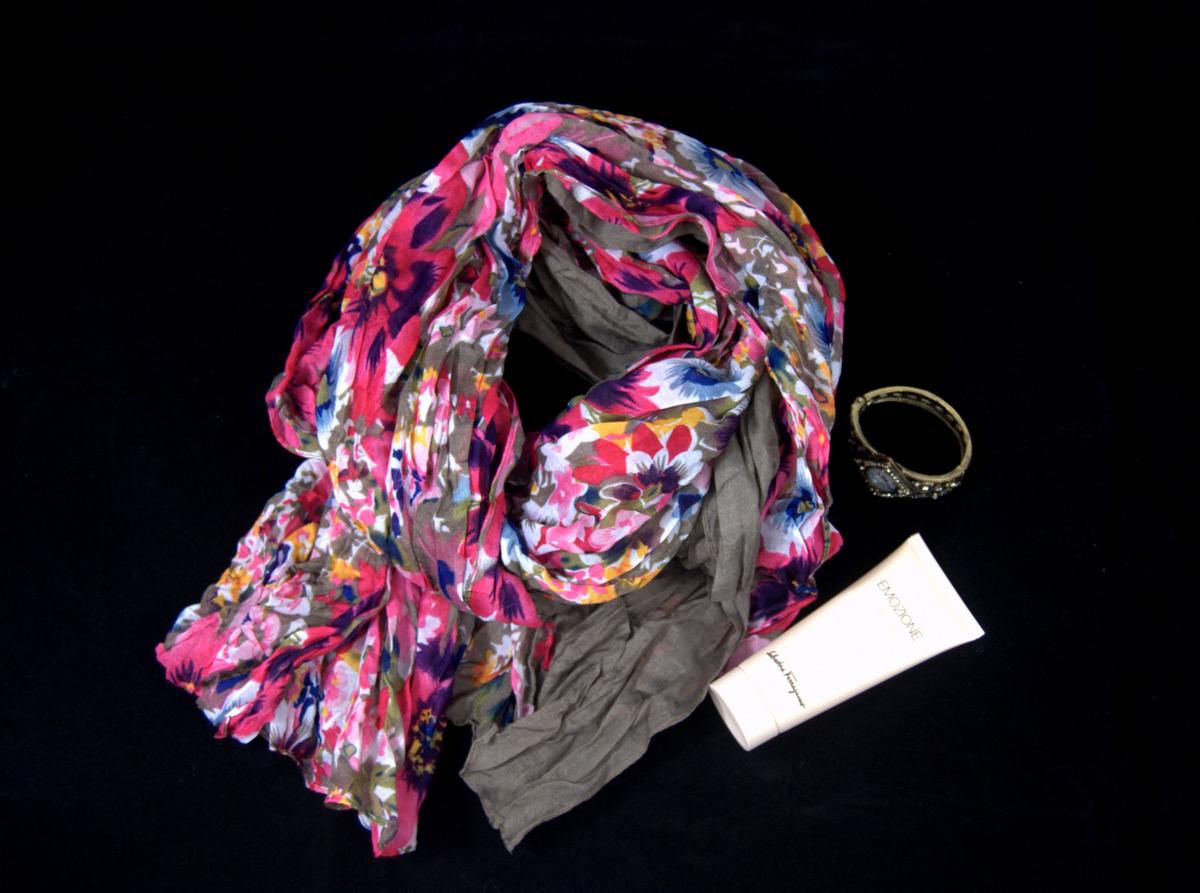 Damski szal w kwiaty z dodatkiem szarej tkaniny, obok bransoletka z kamieniami i tuba kremu na czarnym tle.