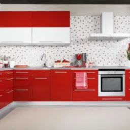 Nowoczesna kuchnia z czerwonymi frontami szafek dolnych i białymi górnymi, mozaika na ścianie nad blatem, dywanik w neutralnym kolorze na podłodze.