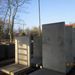 Gotowe elementy betonowe w kształcie litery L, prawdopodobnie do budowy murów oporowych, ustawione jeden za drugim na paletach, z widoczną datą 06/01/2018 w prawym dolnym rogu.