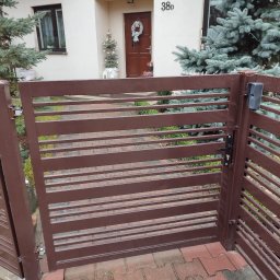 SPAWMET - Brązowa, pozioma brama lamelowa z domofonem na słupku, widok na dom z numerem 38D i świątecznym stroikiem na drzwiach.