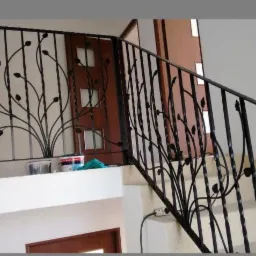 Kuta balustrada schodowa z motywem roślinnym, czarna, z widocznymi puszkami farb i narzędziami malarskimi w tle, sugerującymi prace wykończeniowe.