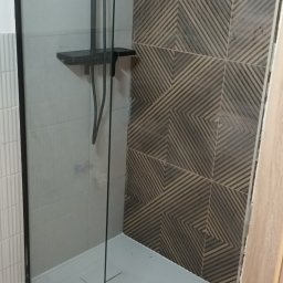 DARKTECH - Nowoczesna kabina prysznicowa z czarną armaturą i geometrycznymi płytkami. Szklana ściana kabiny z czarną ramą. Minimalistyczny design, jasne płytki podłogowe.