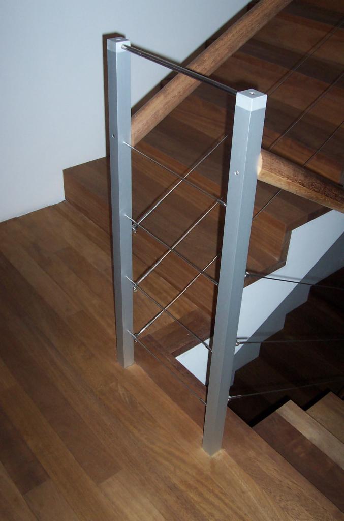 Drewniane schody z nowoczesną balustradą z metalowymi linkami i aluminiowymi słupkami. Widok z dołu, podkreślający detale wykończenia.