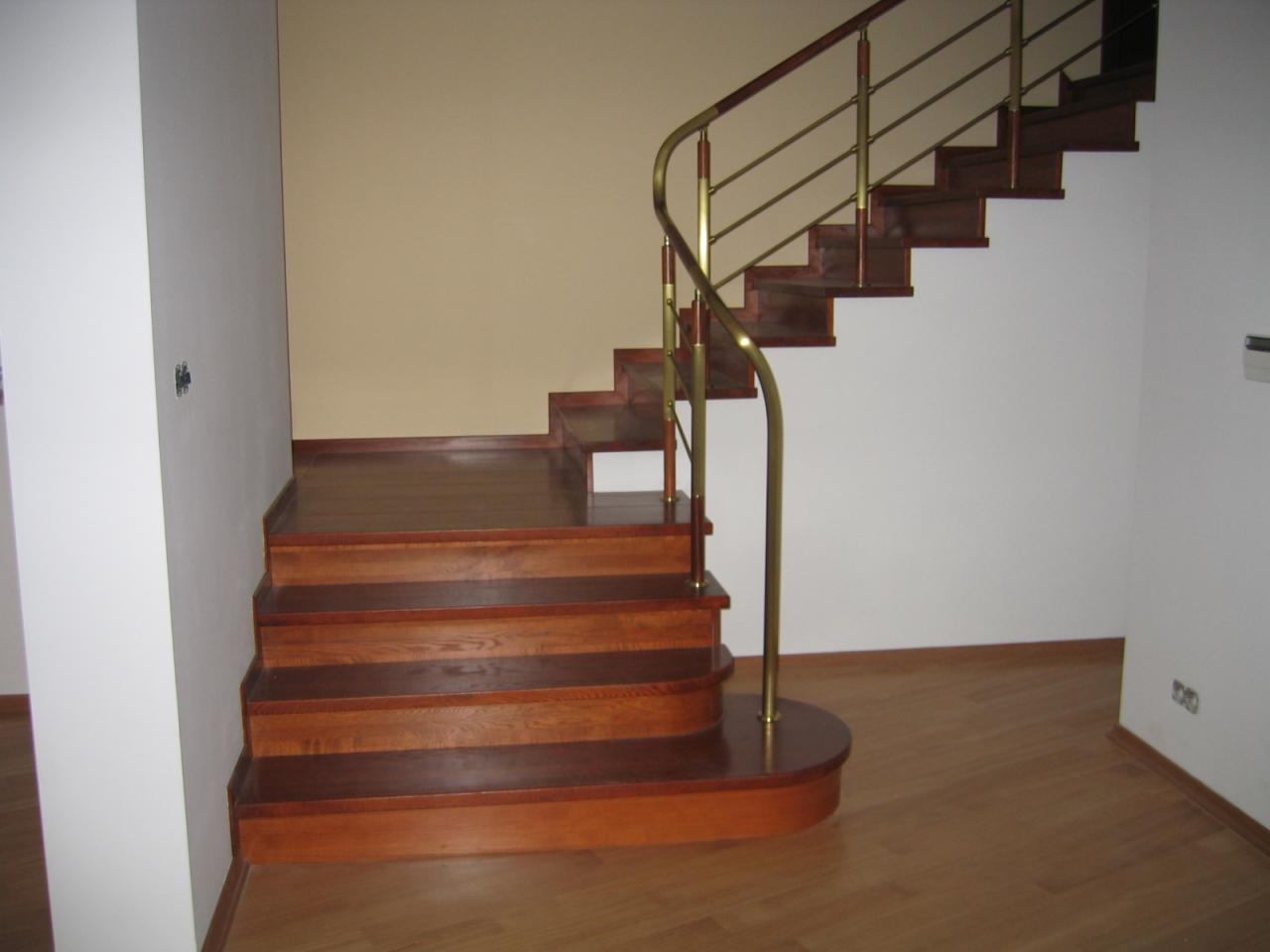 Drewniane schody z metalową balustradą w jasnym wnętrzu. Stopnie w ciepłym odcieniu brązu, podłoga parkietowa. Minimalistyczny design.