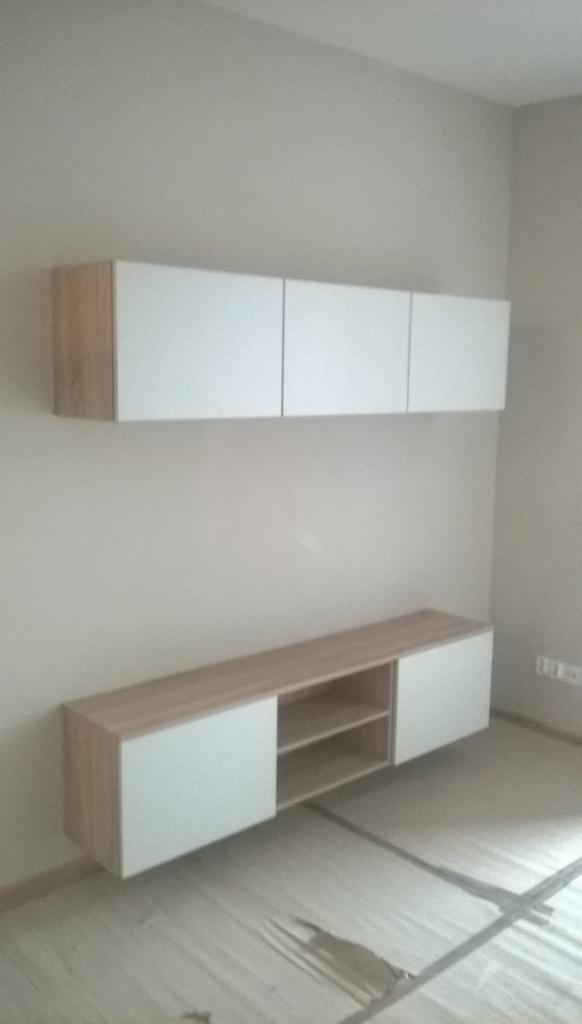 Nowoczesna zabudowa ścienna z szafkami wiszącymi i półkami w odcieniach bieli i drewna, minimalistyczny design, jasne wnętrze, widok z dołu, folia ochronna na podłodze.