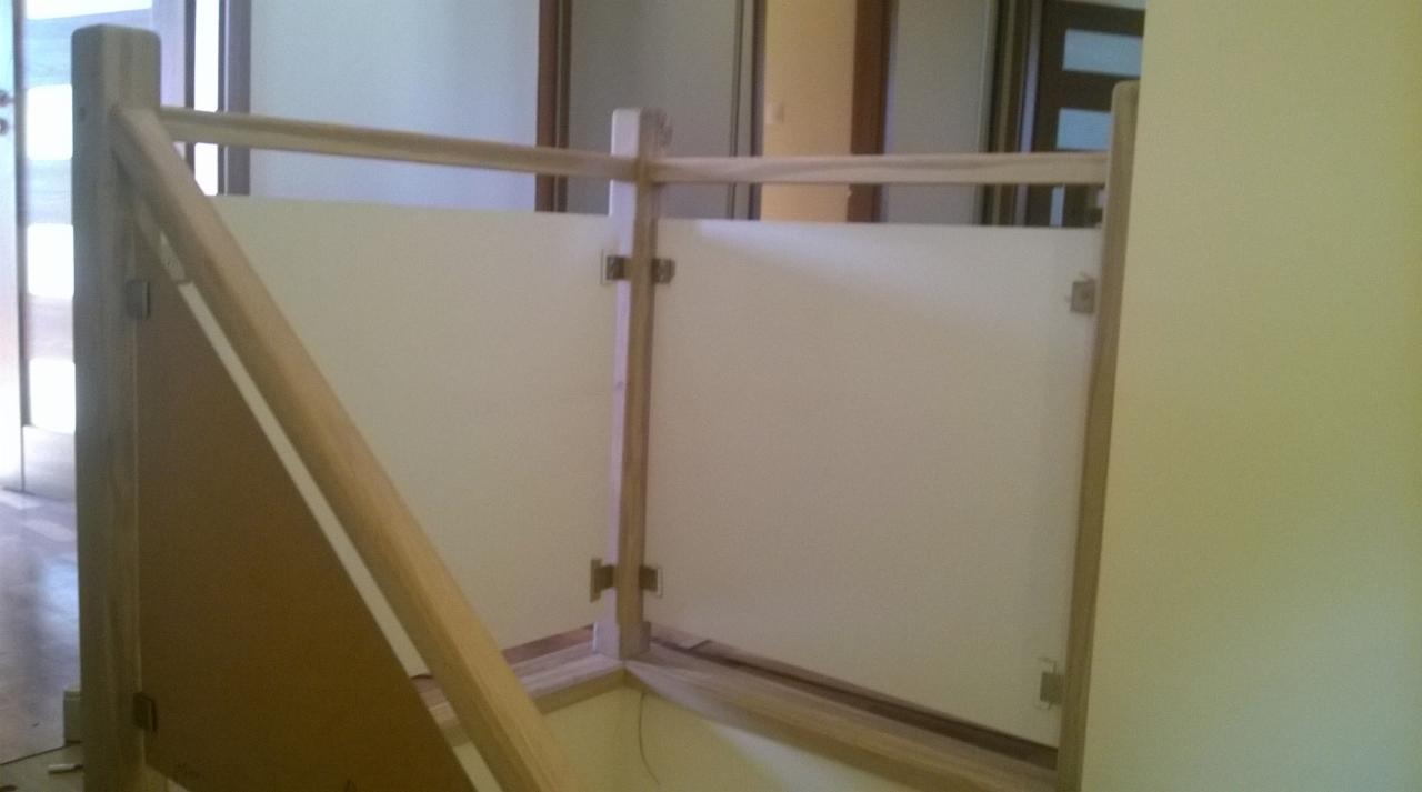 Drewniana balustrada schodowa z białymi panelami, mocowana na metalowych zawiasach. Widoczne elementy konstrukcyjne i fragment podłogi.