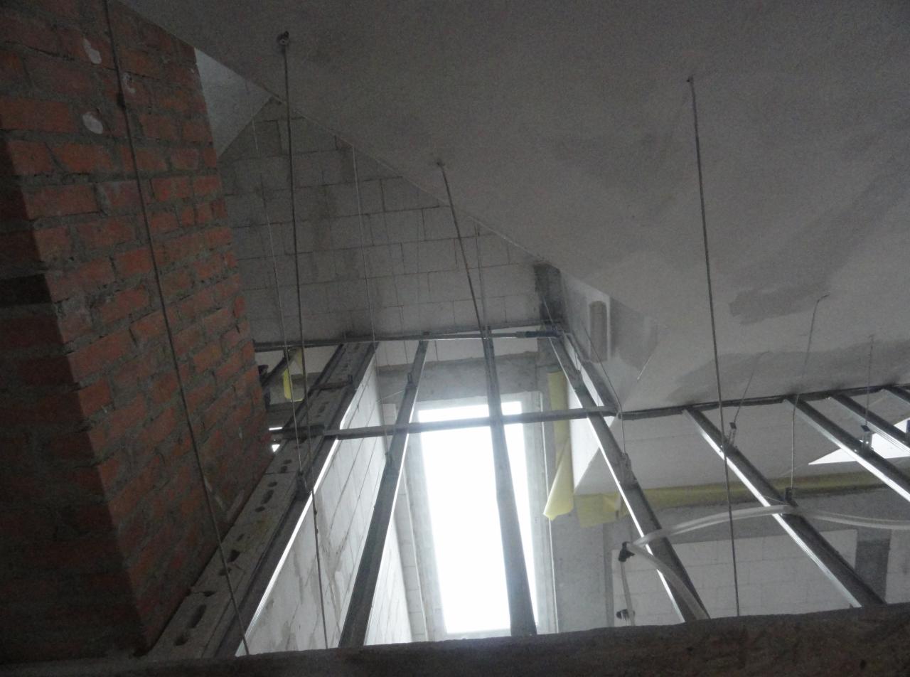 Poddasze w trakcie wykończenia: widok na konstrukcję metalową sufitu, częściowo ocieplone ściany i ceglany komin w surowym stanie.