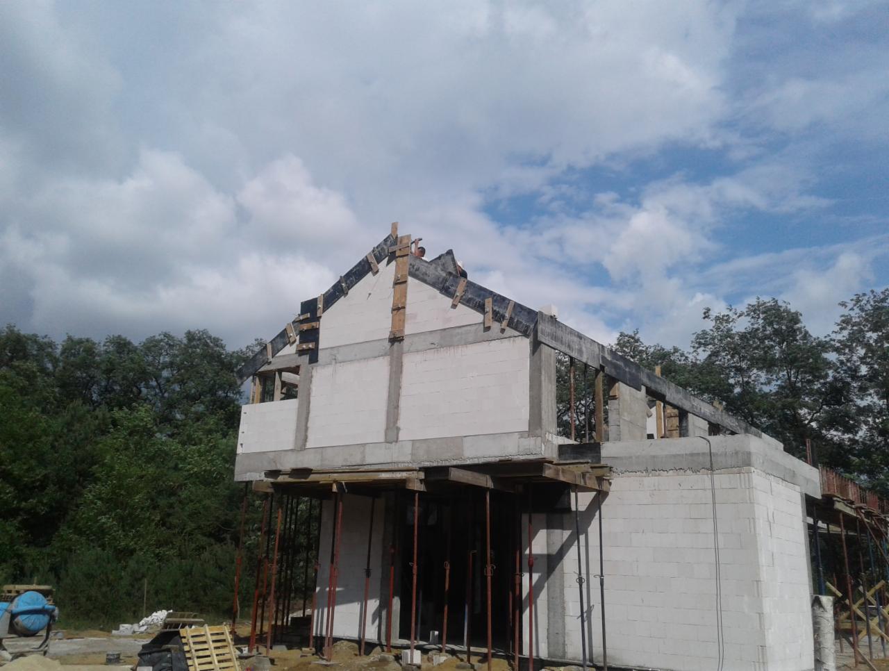 Budowa domu jednorodzinnego w Przysusze na etapie wznoszenia ścian z bloczków i przygotowania pod wieniec, widoczne szalunki i podpory.